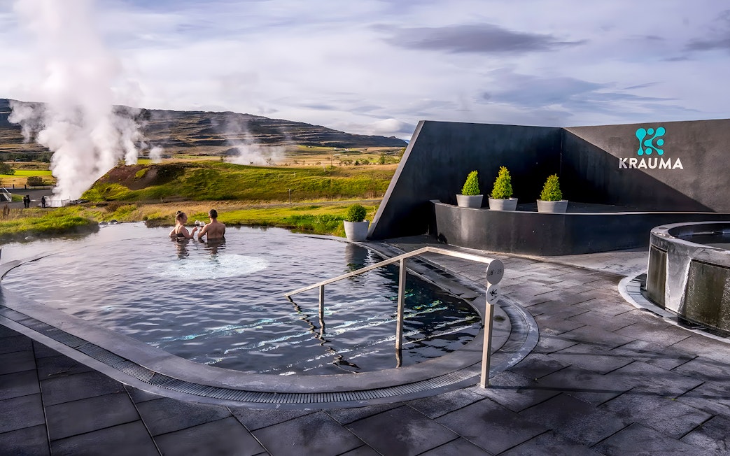 Visitors relaxing in Krauma Geothermal Baths with steam rising in the Icelandic landscape.