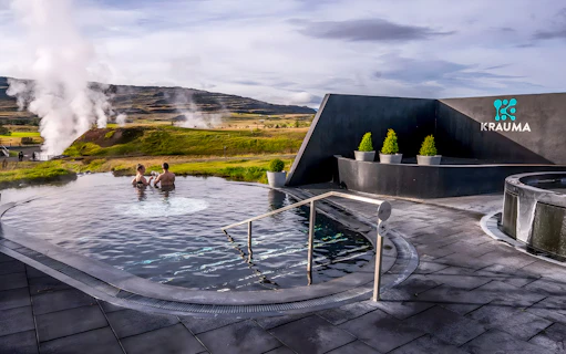 Visitors relaxing in Krauma Geothermal Baths with steam rising in the Icelandic landscape.