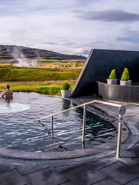 Visitors relaxing in Krauma Geothermal Baths with steam rising in the Icelandic landscape.