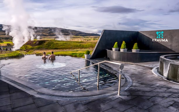 Visitors relaxing in Krauma Geothermal Baths with steam rising in the Icelandic landscape.