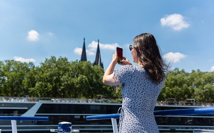 Person photographing Cologne Cathedral spires from a boat on the Rhine River.