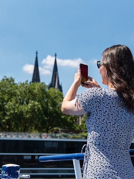 Person photographing Cologne Cathedral spires from a boat on the Rhine River.