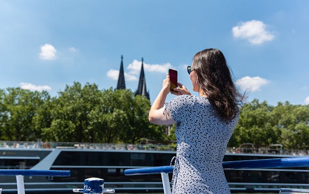 Person photographing Cologne Cathedral spires from a boat on the Rhine River.