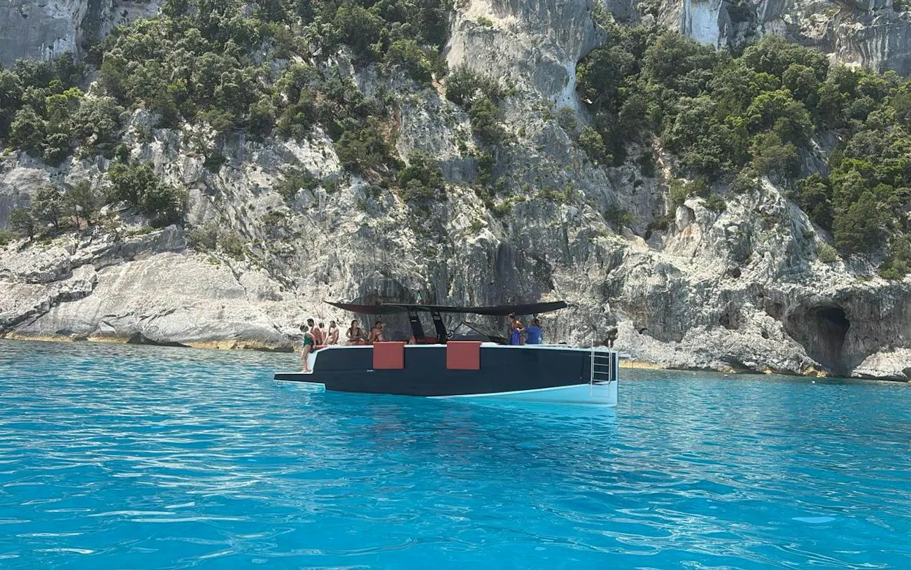 Mini yacht with passengers near rocky cliffs in Gulf of Orosei, Cala Gonone, Nuoro.