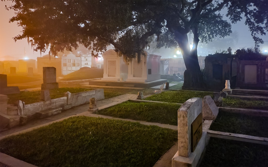 New Orleans cemetery at night with tombstones and trees.