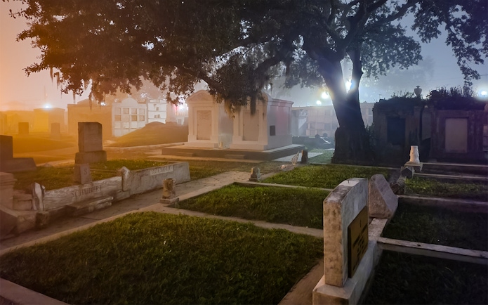 New Orleans cemetery at night with tombstones and trees.