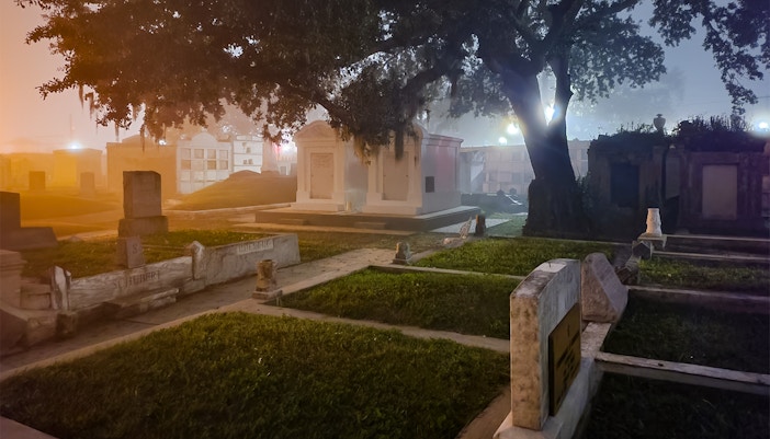 New Orleans cemetery at night with tombstones and trees.