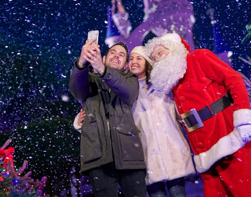 Visitors taking a selfie with Santa Claus at a snowy Christmas event.