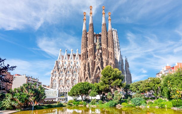Sagrada Familia towers in Barcelona with surrounding greenery and pond.