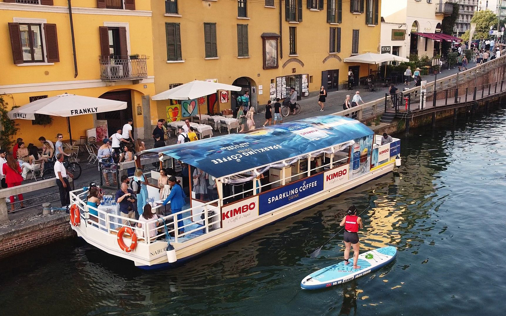 Canal boat with tourists and paddleboarder on Navigli canal in Milan.