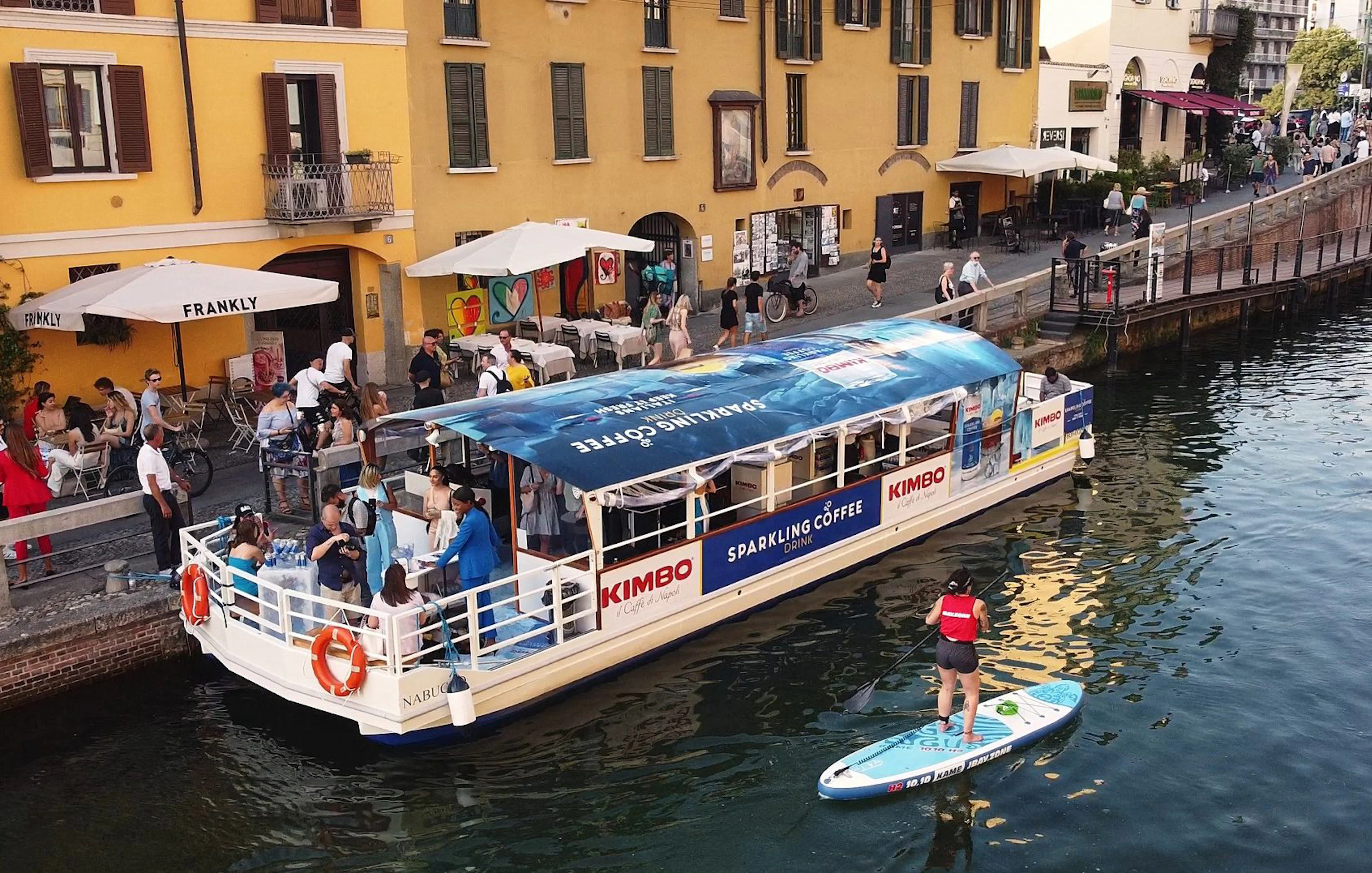 Canal boat with tourists and paddleboarder on Navigli canal in Milan.
