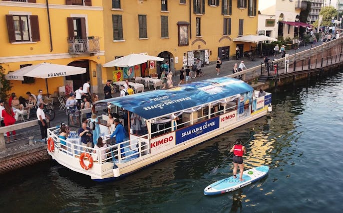 Canal boat with tourists and paddleboarder on Navigli canal in Milan.