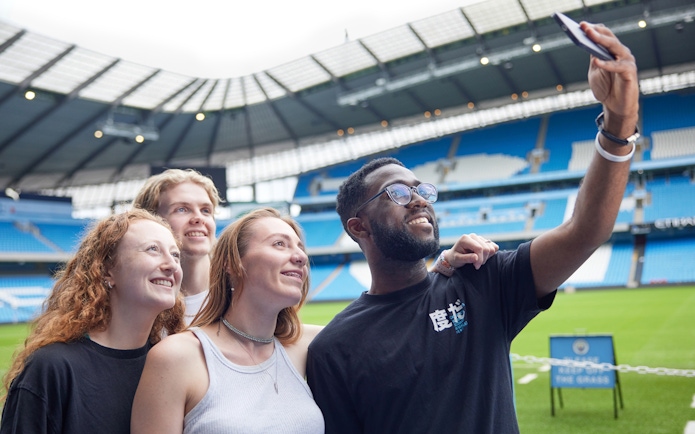 Participants taking a selfie on the field of Manchester City Stadium.