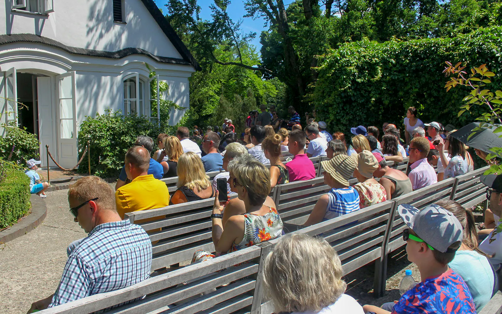 Visitors seated outside Fryderyk Chopin's birthplace in Poland, surrounded by greenery.