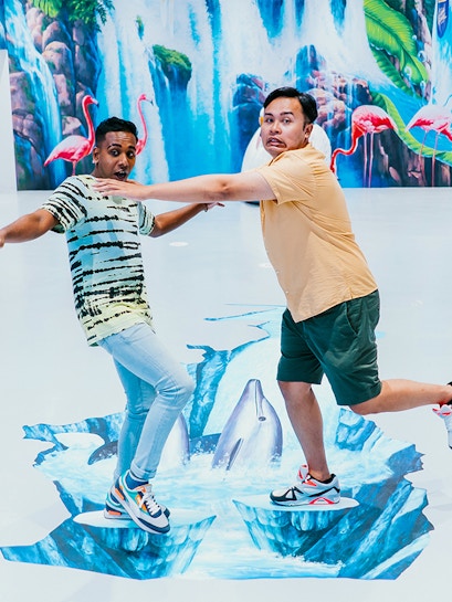 Visitors interacting with 3D art at Trick Eye Museum, featuring dolphins and waterfalls.