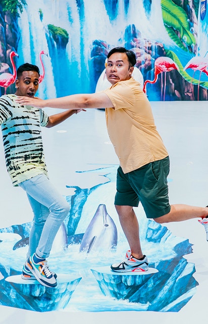 Visitors interacting with 3D art at Trick Eye Museum, featuring dolphins and waterfalls.