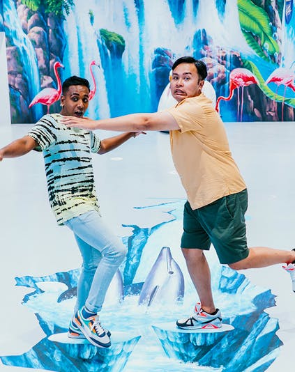 Visitors interacting with 3D art at Trick Eye Museum, featuring dolphins and waterfalls.