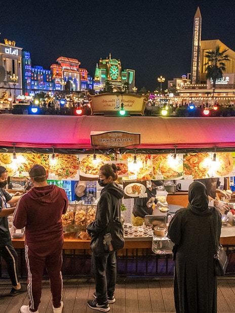Floating market stall with visitors at Global Village Dubai, illuminated buildings in the background.