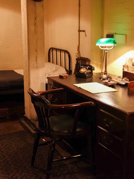 Desk and bed in Churchill War Rooms, London, featuring vintage phone and lamp.