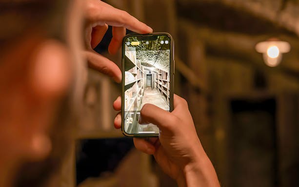 Person photographing historical pharmacy cellar shelves on a smartphone.