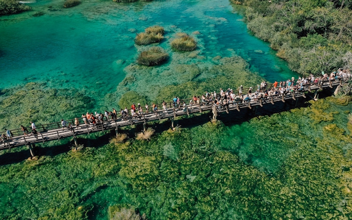 Visitors on a wooden bridge over turquoise waters at Krka National Park, Croatia.