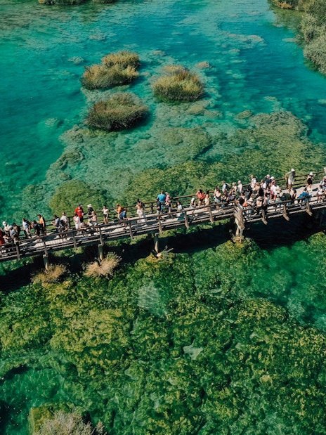 Visitors on a wooden bridge over turquoise waters at Krka National Park, Croatia.