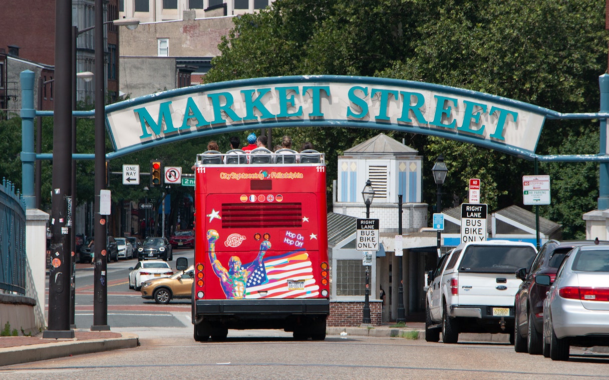 Red double-decker bus on Philadelphia Hop-On-Hop-Off Tour passing under Market Street sign.