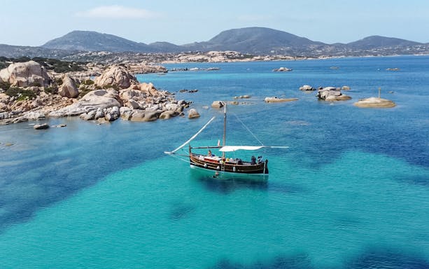 Wooden sailboat on clear blue waters near Asinara Island, Italy.