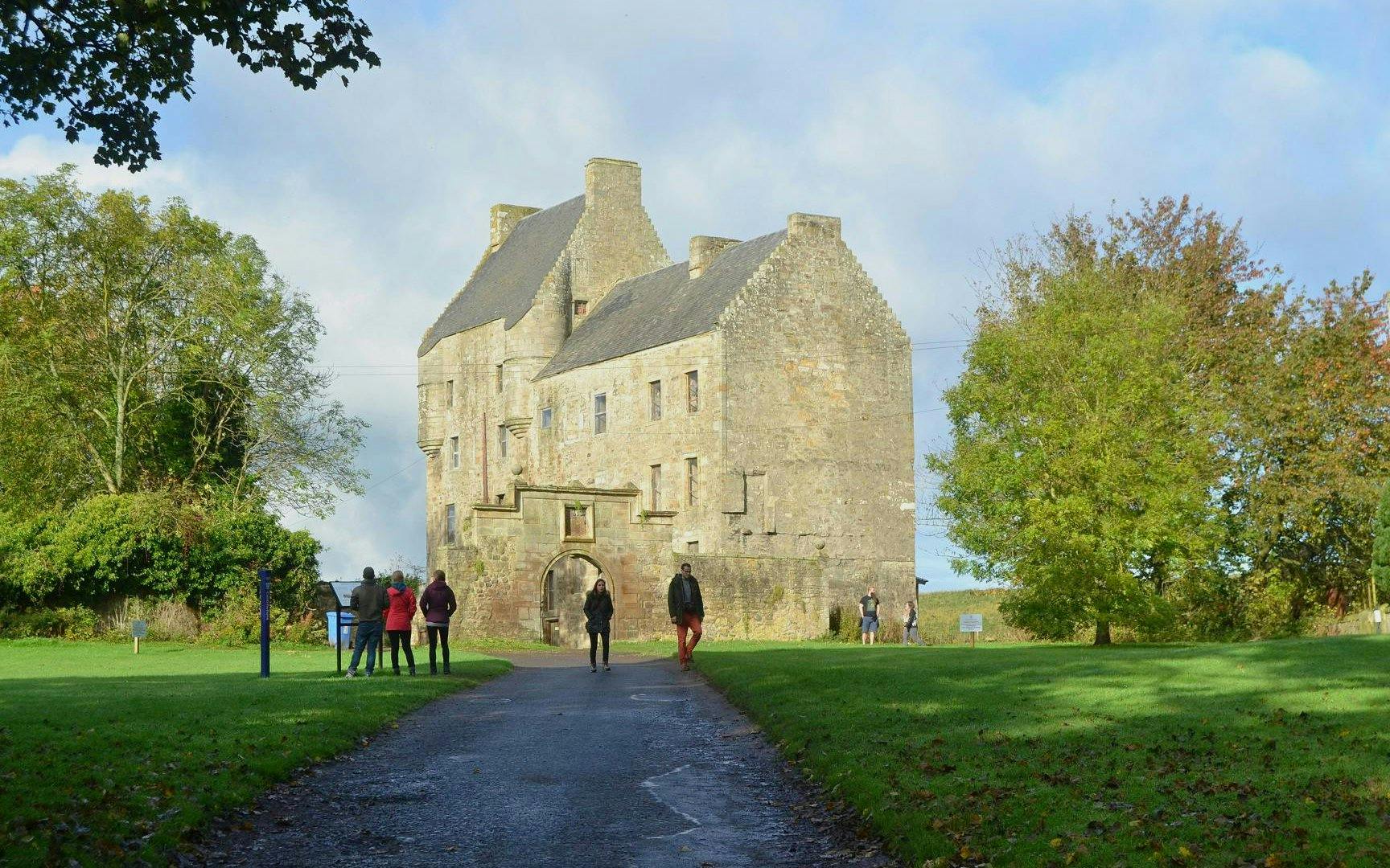 Visitors walking towards Midhope Castle in Scotland, surrounded by green trees and a clear sky.