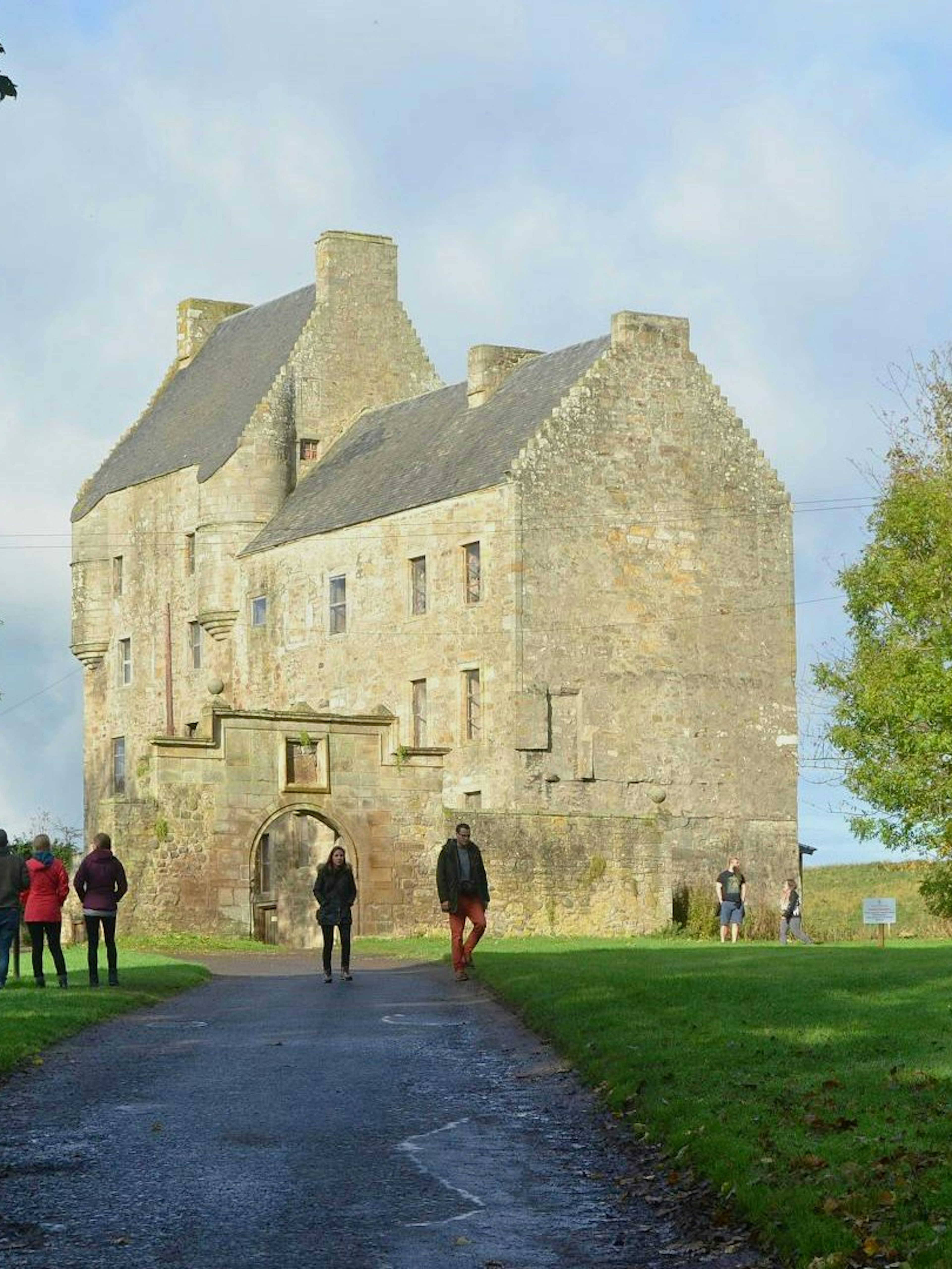 Visitors walking towards Midhope Castle in Scotland, surrounded by green trees and a clear sky.