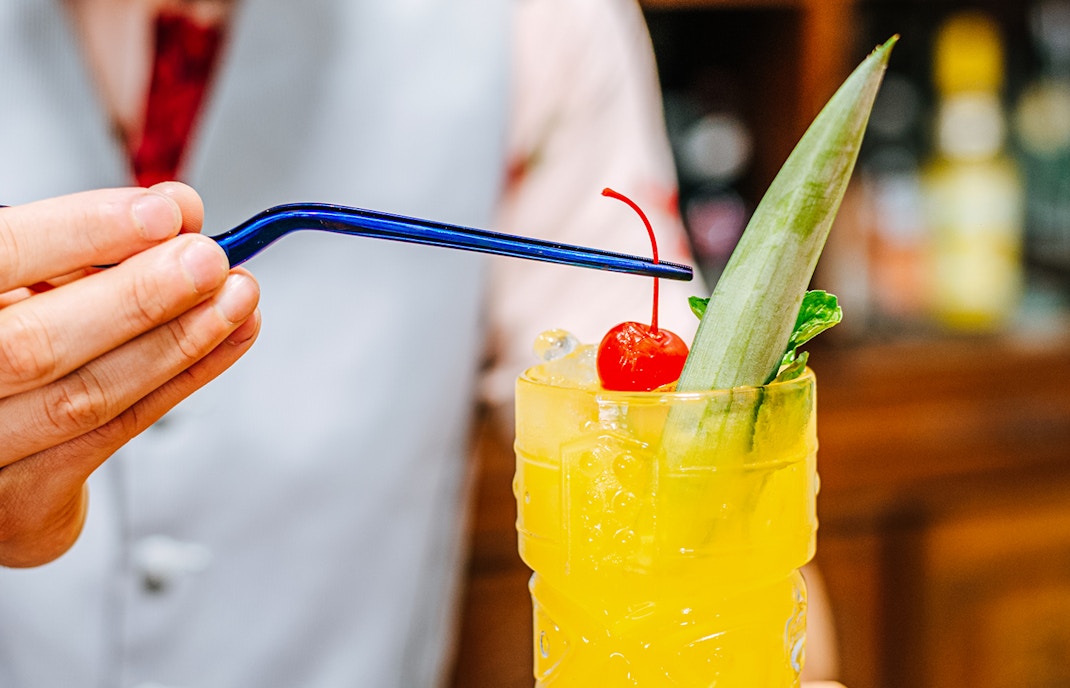 Bartender garnishing tiki cocktail with a cherry.