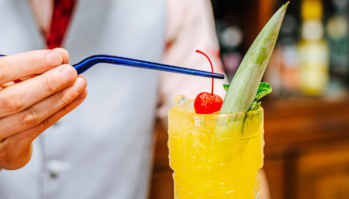 Bartender garnishing tiki cocktail with a cherry.