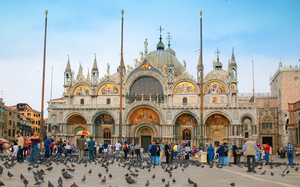 St. Mark's Basilica facade with tourists and pigeons in Venice, Italy.