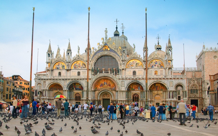 St. Mark's Basilica facade with tourists and pigeons in Venice, Italy.