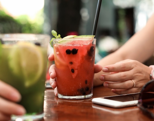Hands holding a glass of fruit juice with berries and mint on a wooden table.
