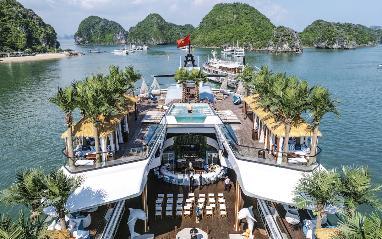 Aerial view of cruise deck with pool and palm trees, surrounded by limestone islands in Halong Bay.