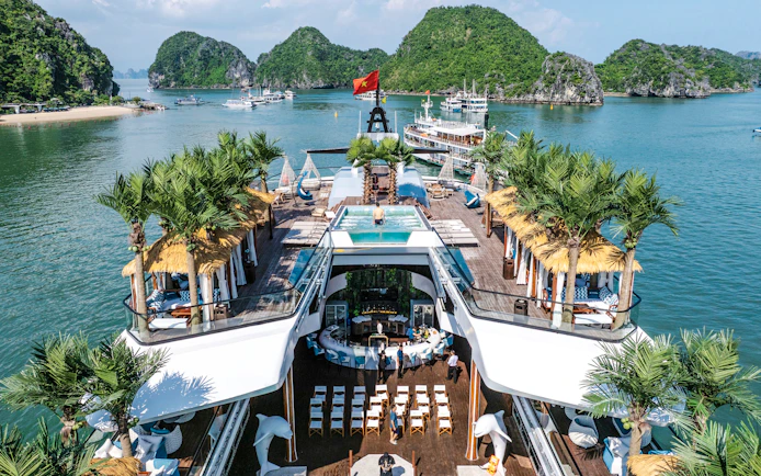 Aerial view of cruise deck with pool and palm trees, surrounded by limestone islands in Halong Bay.