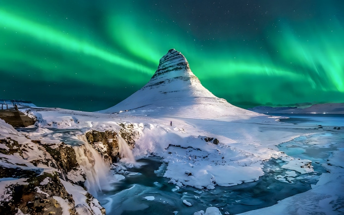 Northern lights over snow-covered mountain and waterfall in Tromso, Norway.