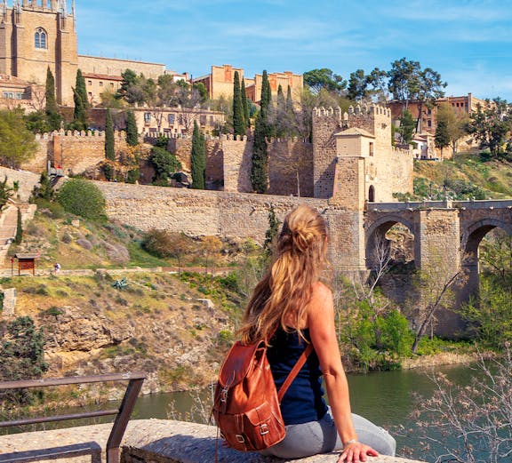 Woman sitting by the Tagus River with view of Toledo's medieval walls, Spain.