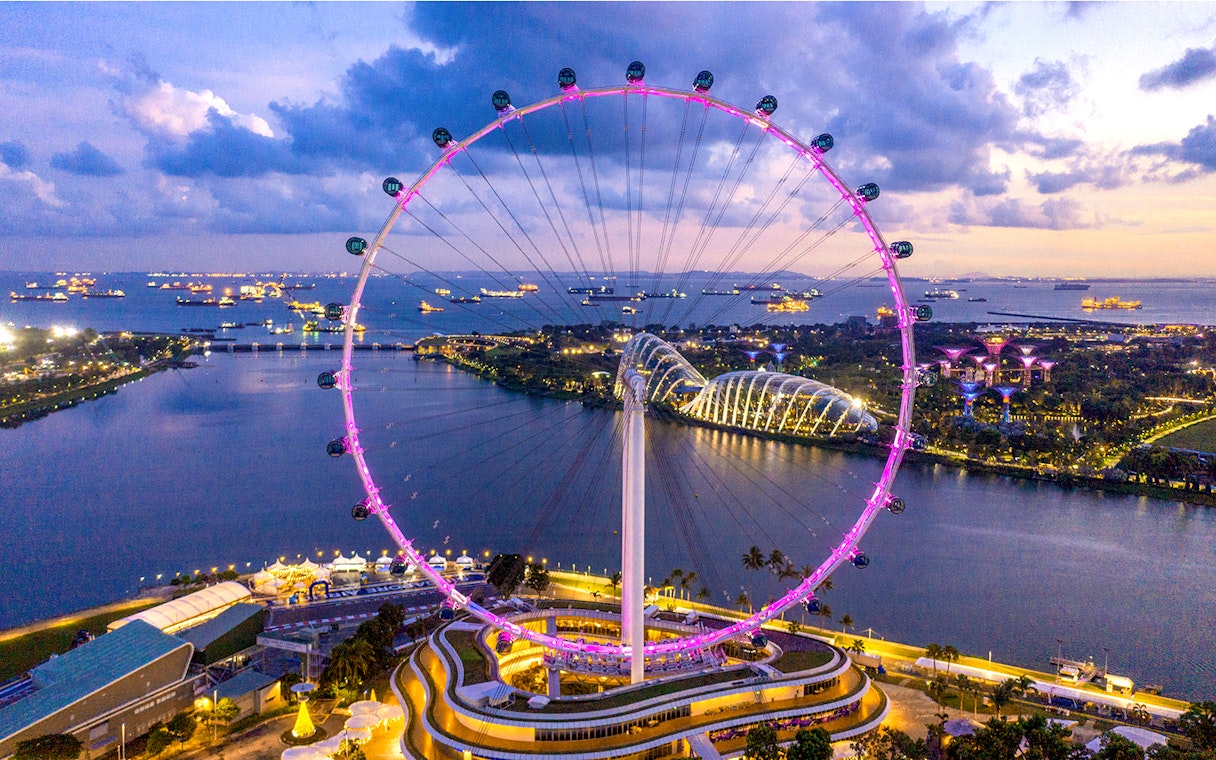 Aerial view of the illuminated Singapore Flyer at dusk with Marina Bay in the background.