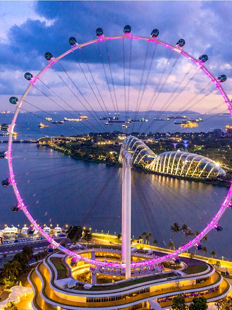 Aerial view of the illuminated Singapore Flyer at dusk with Marina Bay in the background.