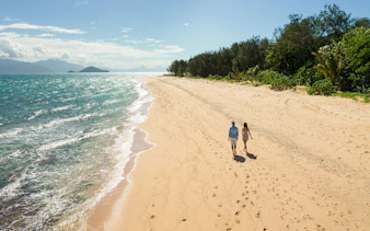 Couple walking along Frankland Islands beach with ocean view.