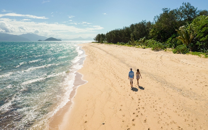 Couple walking along Frankland Islands beach with ocean view.