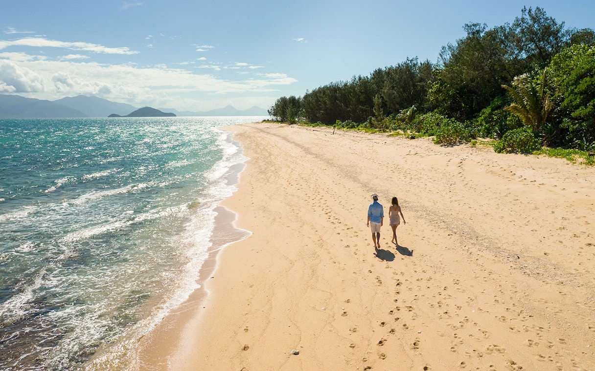 Couple walking along Frankland Islands beach with ocean view.