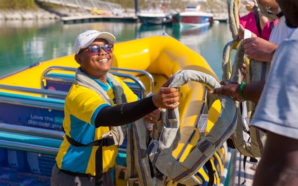 Tour guide handing life jackets to guests on Al Marjan Island speed boat tour.