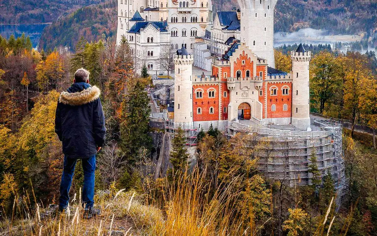 Person overlooking Neuschwanstein Castle surrounded by autumn trees in Bavaria, Germany.