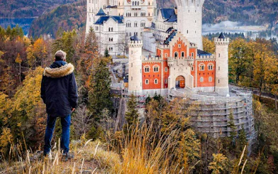 Person overlooking Neuschwanstein Castle surrounded by autumn trees in Bavaria, Germany.