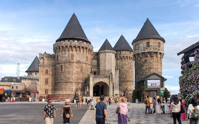 Stone castle towers at Ba Na Hills with tourists exploring the courtyard.