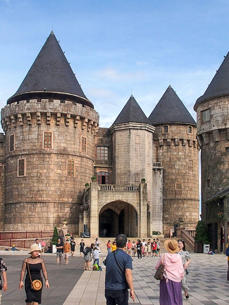 Stone castle towers at Ba Na Hills with tourists exploring the courtyard.