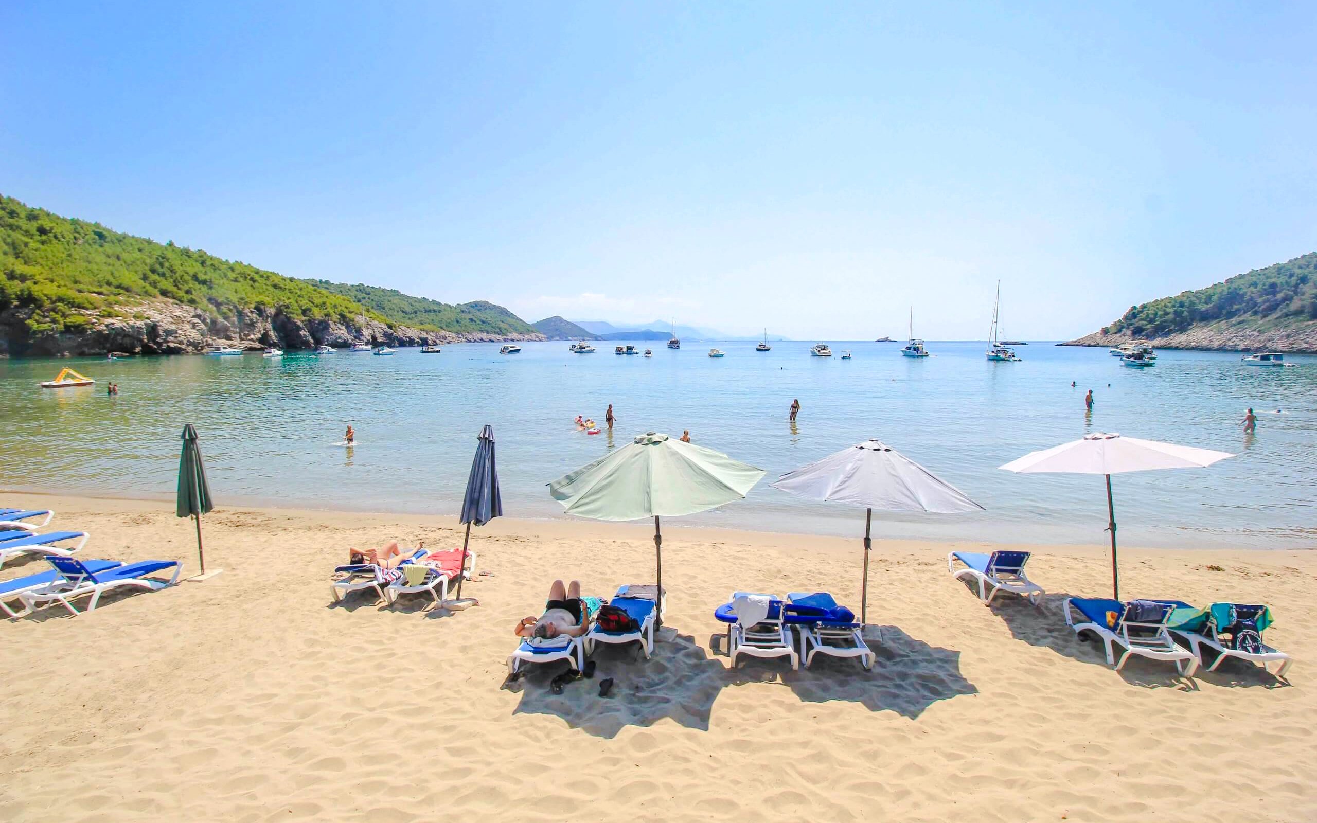 Sunbathers and umbrellas on Šunj Beach with boats in the bay, Lopud Island, Croatia.
